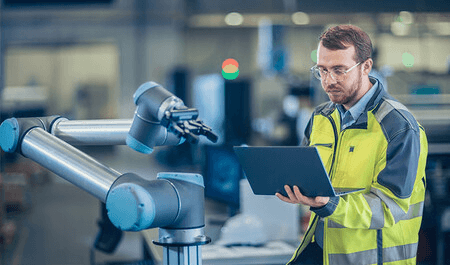 Professional engineer in safety vest operating robotic arm equipment with laptop for automation control