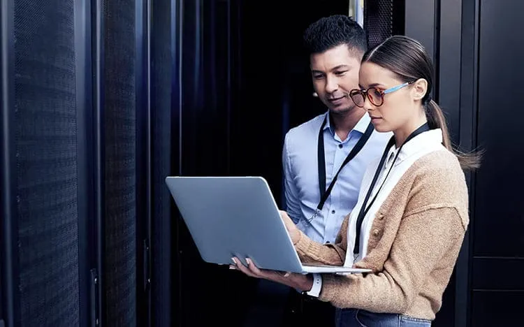 Professional IT professionals reviewing laptop computer in modern data center server room environment for automation
